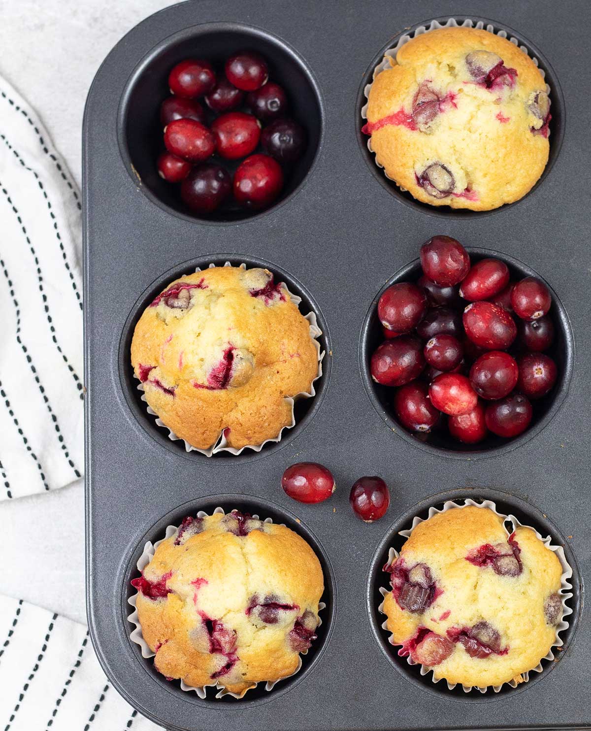 Cranberry Muffins in a muffin tin along with fresh Cranberries