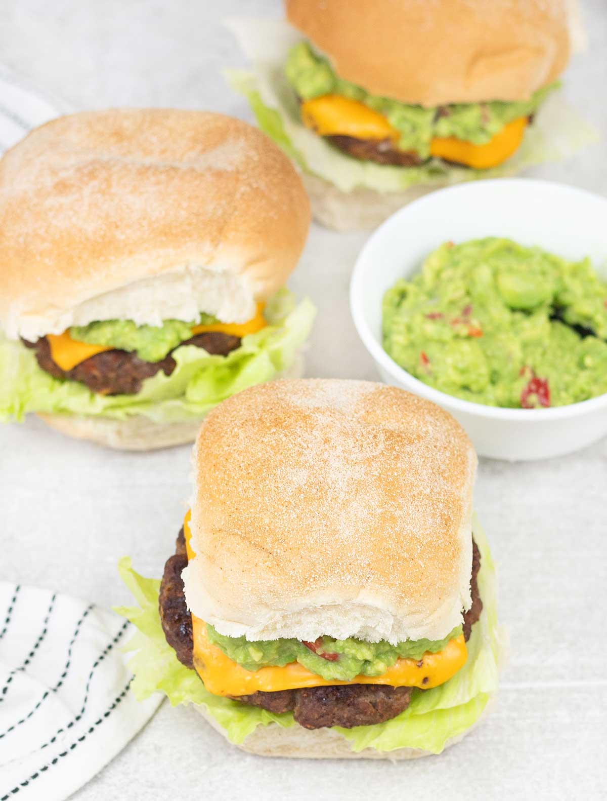 3 Mexican cheeseburgers and a small bowl of guacamole.