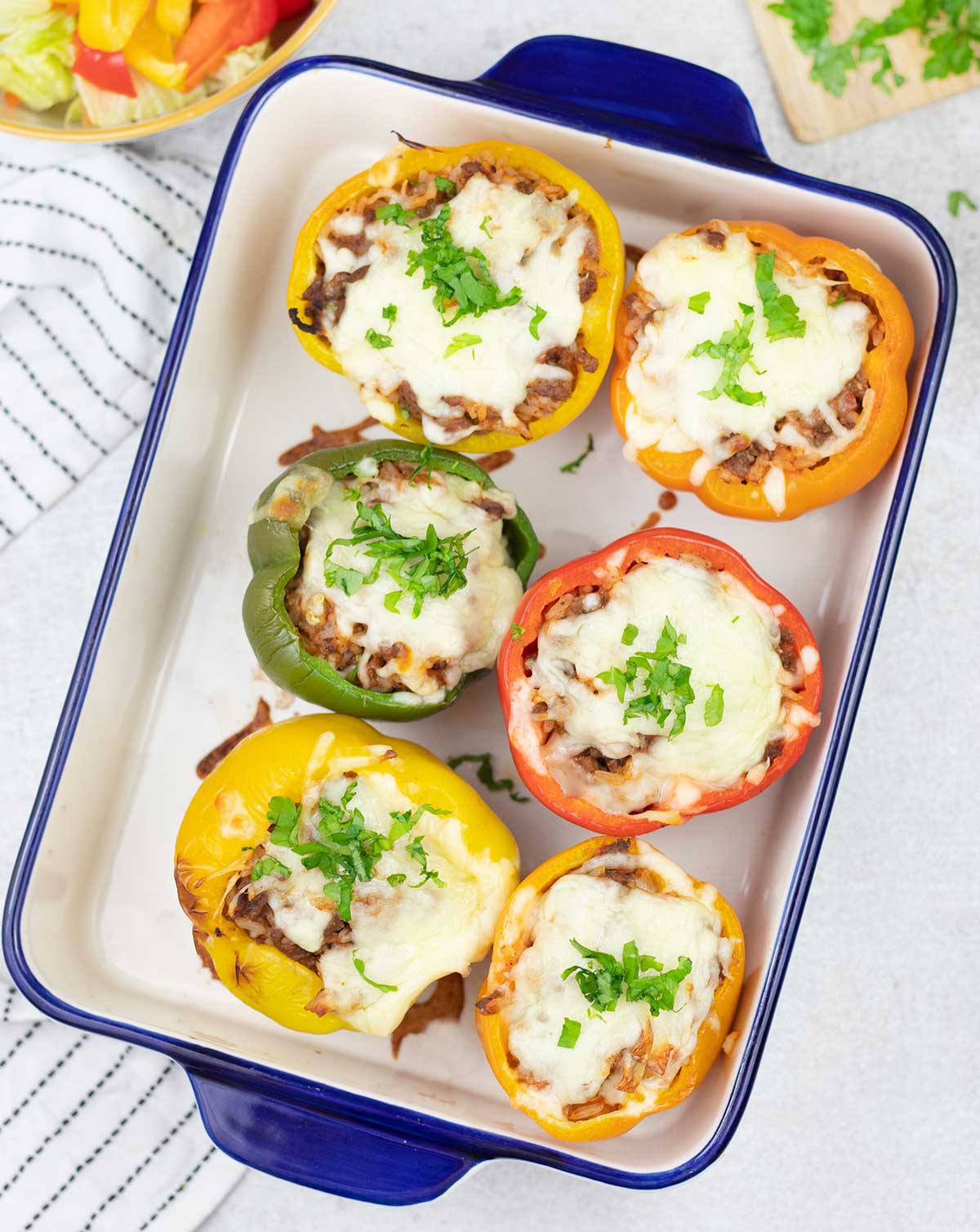 Baked stuffed bell peppers with rice and ground beef in a baking pan.