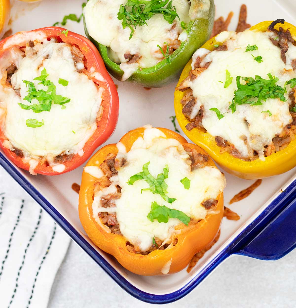 Baked stuffed bell peppers with rice and ground beef in a baking pan.