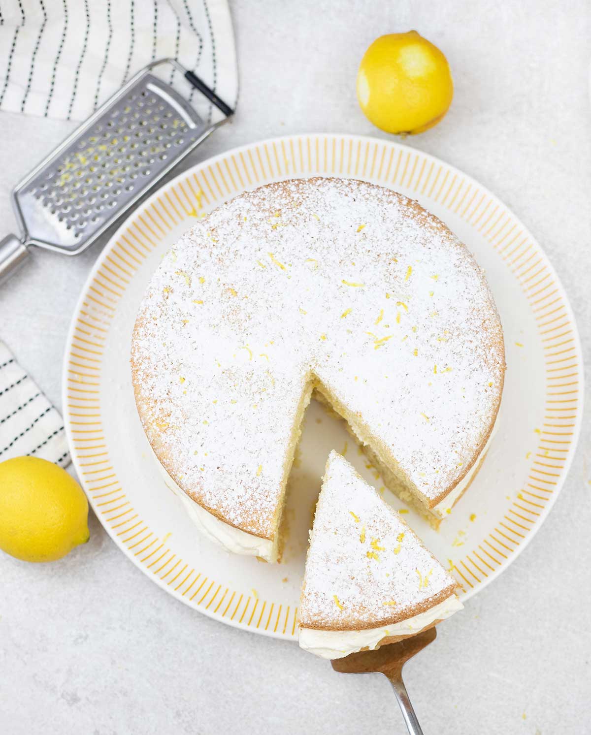 Lemon Victoria sponge and some lemons are in the background.
