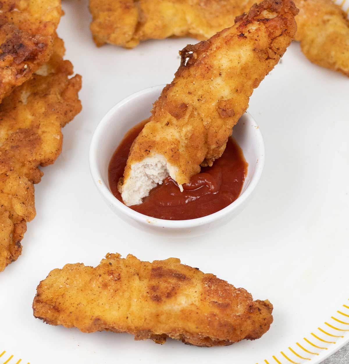 Fried chicken fingers dipped in a bowl of ketchup.