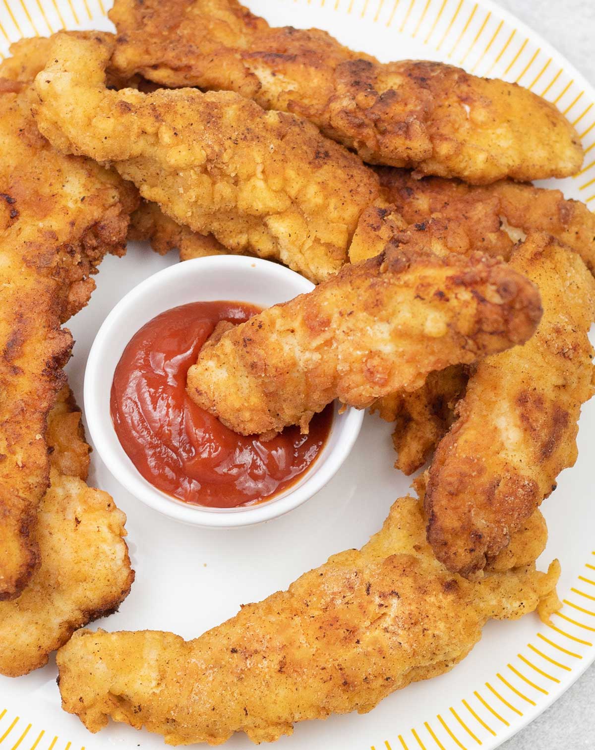 Fried chicken fingers dipped in a bowl of ketchup.