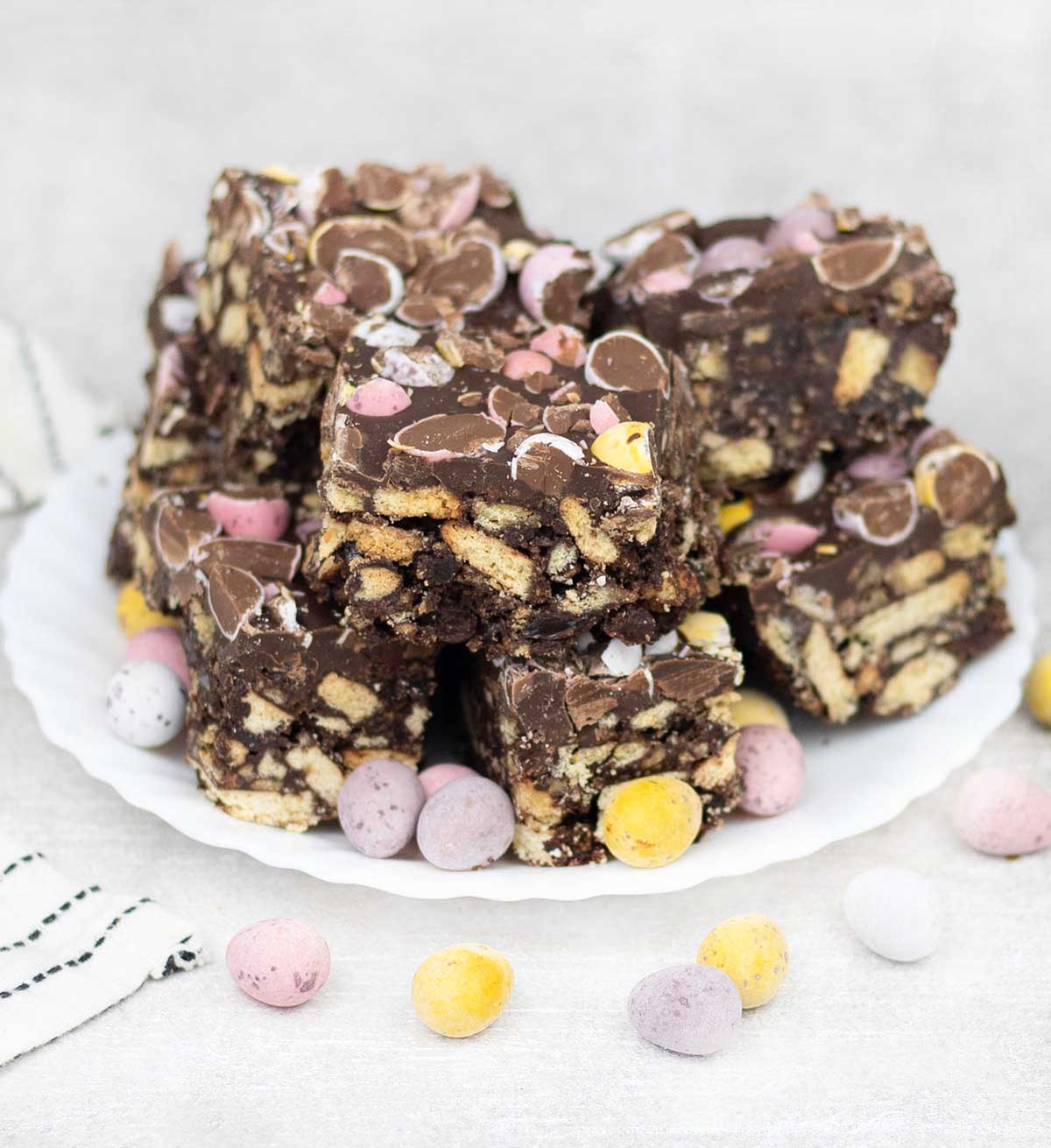 Slices of chocolate Easter tiffin studded with mini eggs on a a plate.