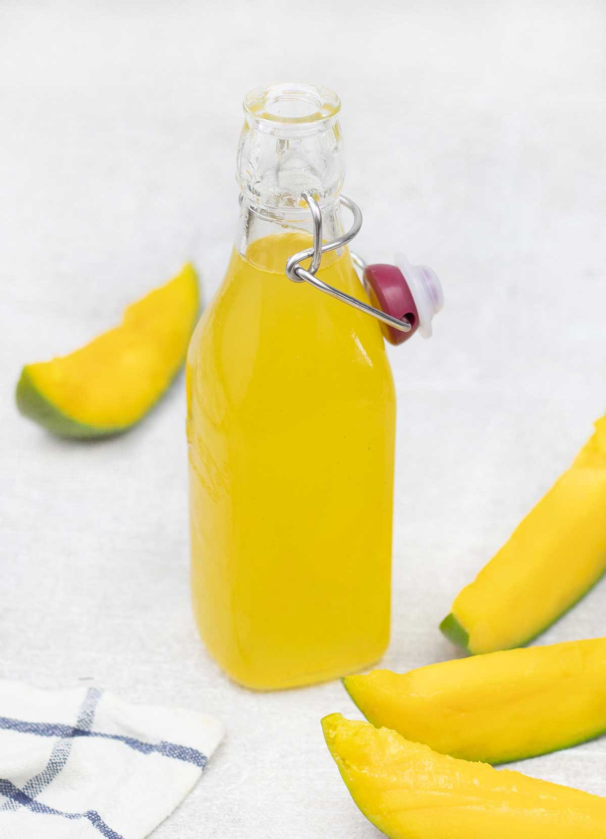 Mango syrup in a glass bottle and some mango slices around it.