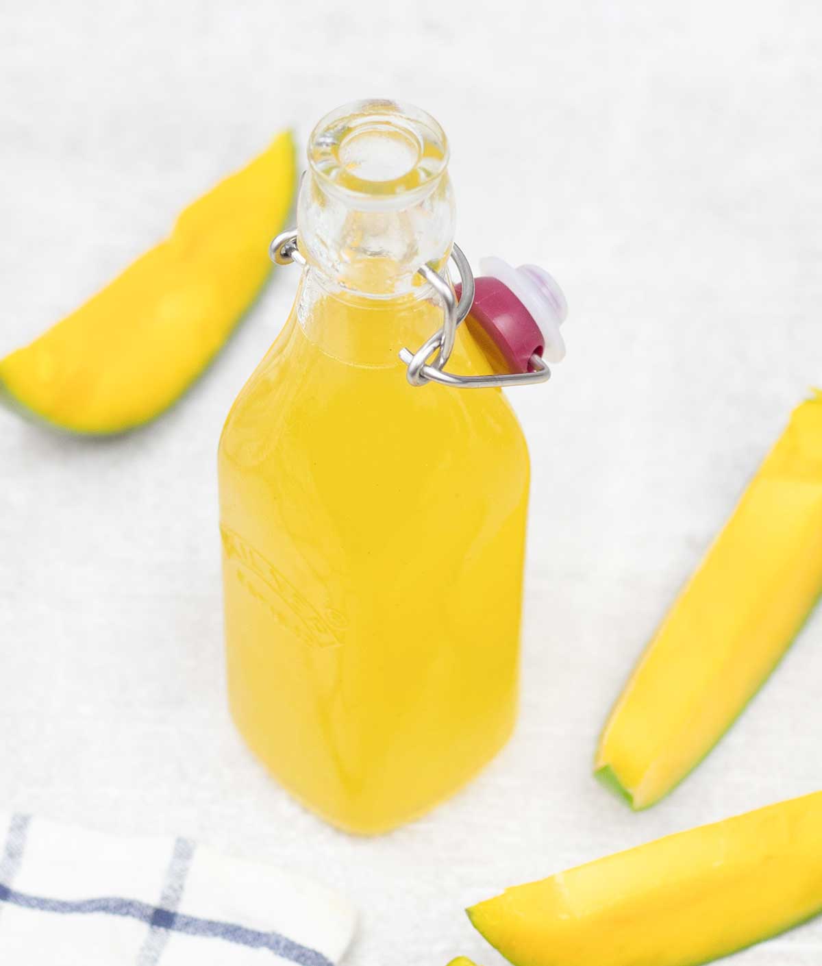 Mango syrup in a glass bottle and some mango slices around it.