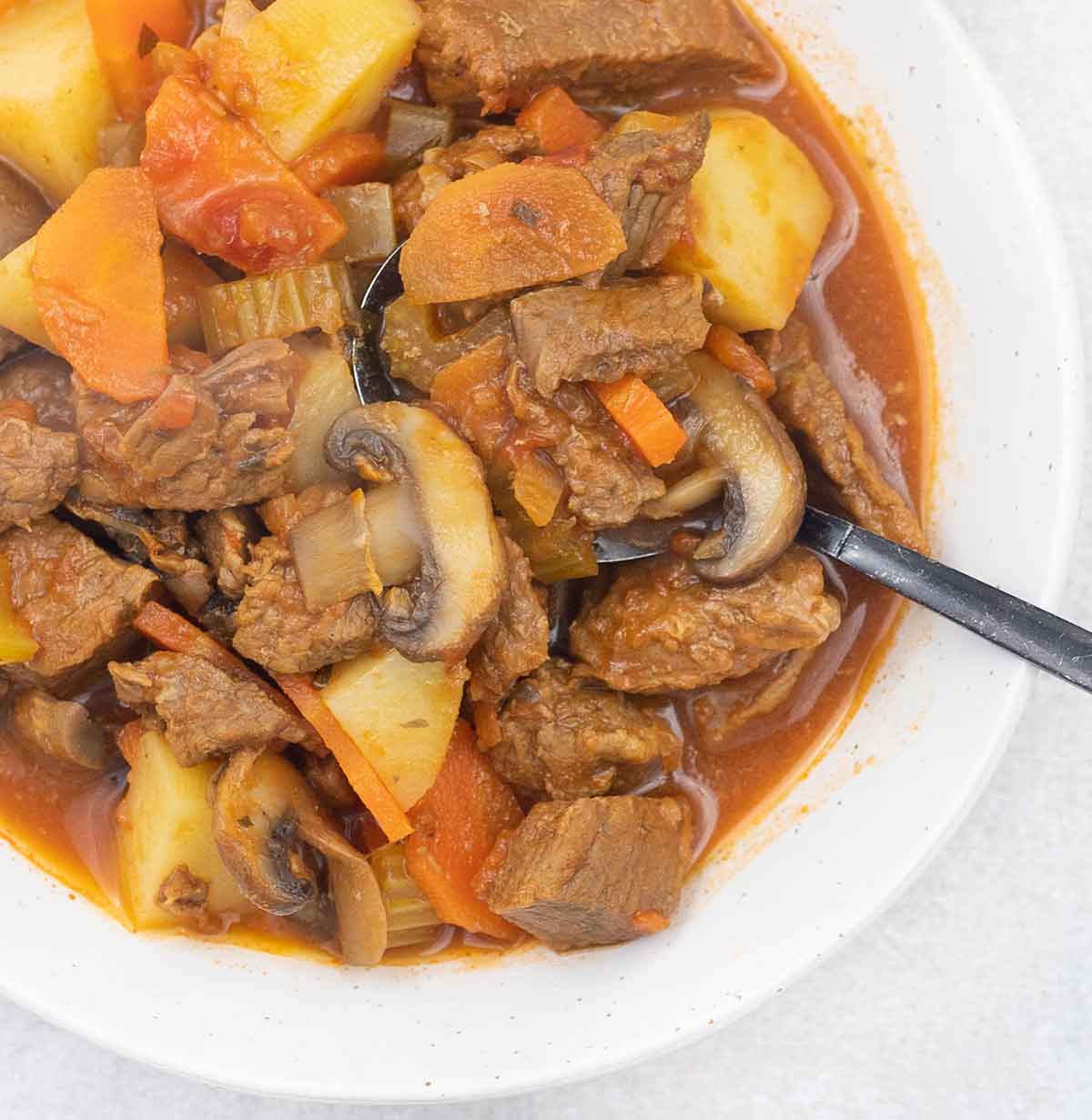 A spoonful of beef stew with tomato sauce.