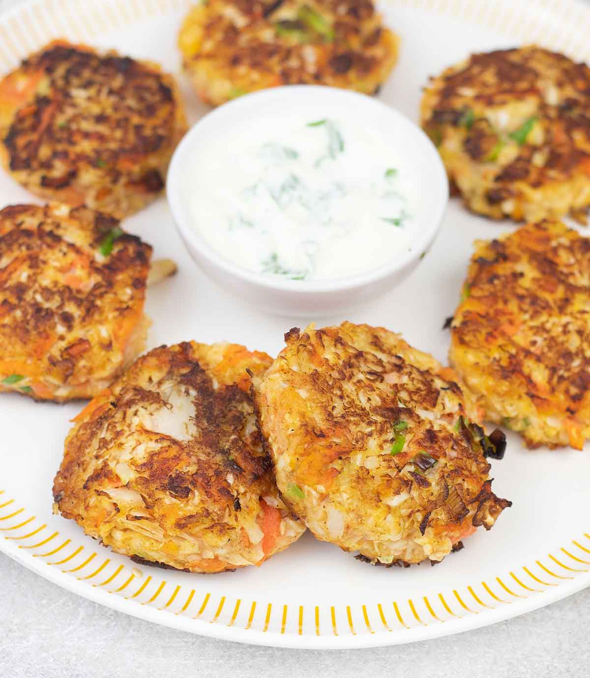 Cabbage fritters on a serving plate and a bowl of sour cream sauce.