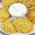 zucchini pancakes on a serving plate and a bowl of sour cream sauce.