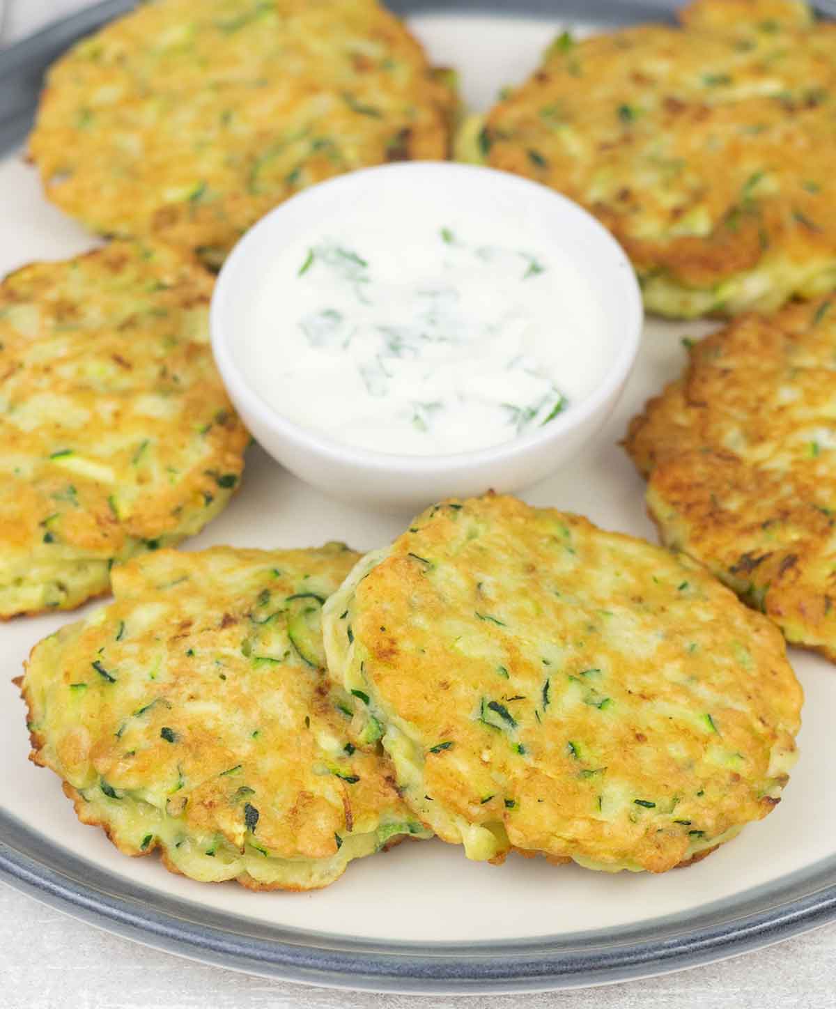 zucchini pancakes on a serving plate and a bowl of sour cream sauce.