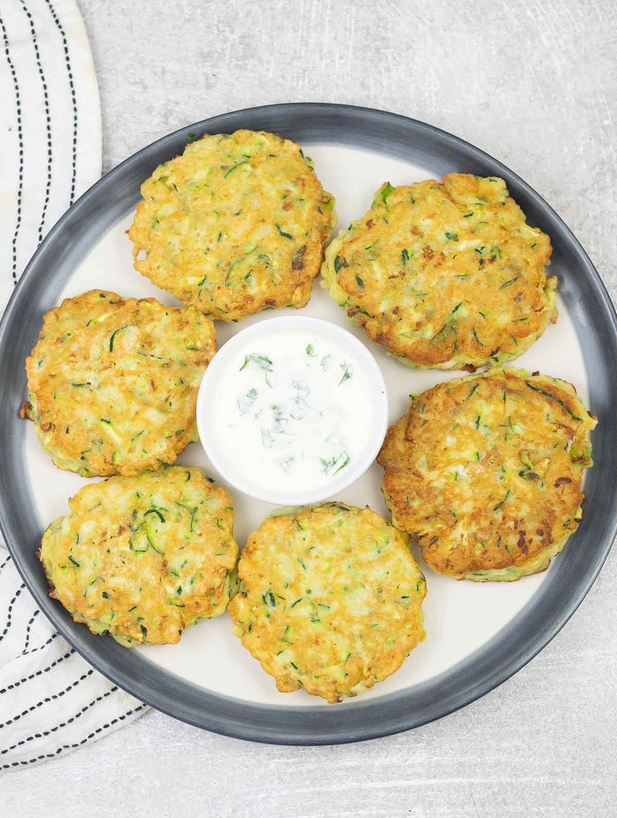 Zucchini pancakes on a serving plate and a bowl of sour cream sauce.