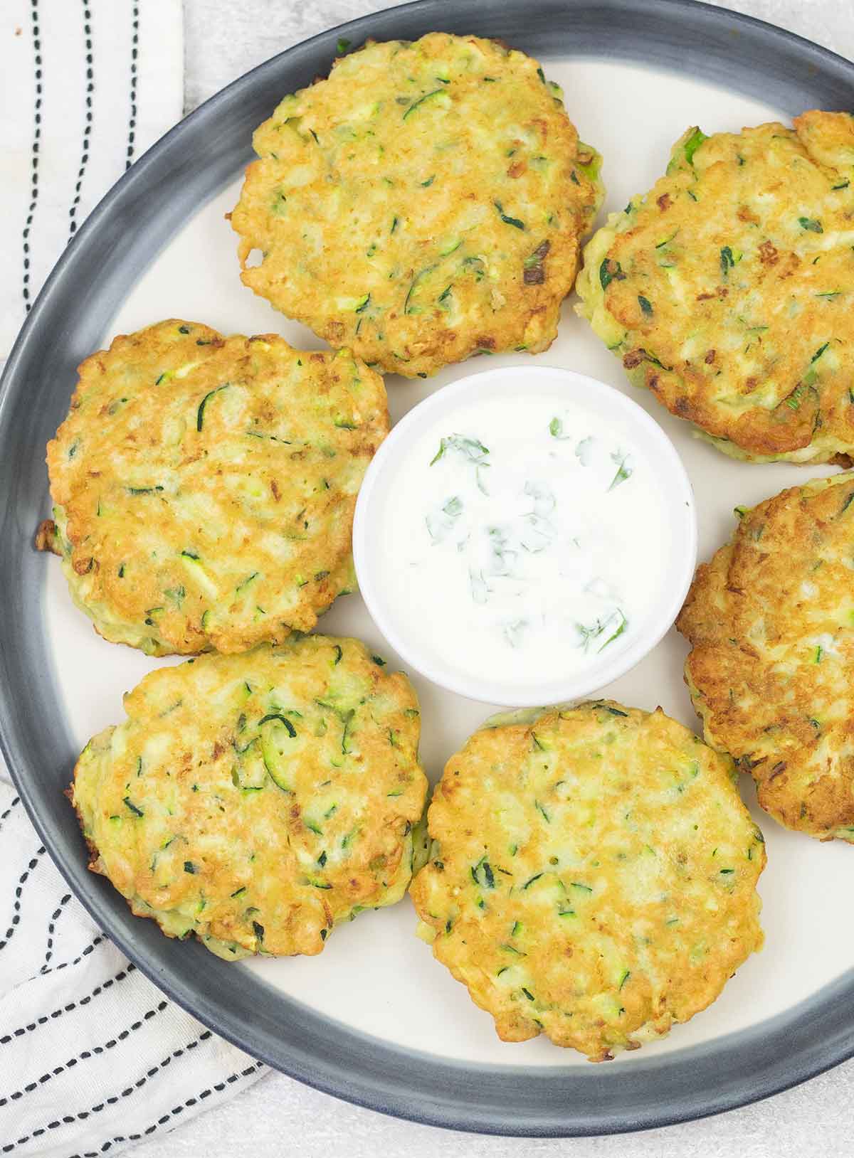 Zucchini pancakes on a serving plate and a bowl of sour cream sauce.
