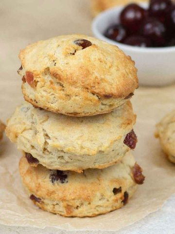 3 cherry scones on top of each others and a bowl of glacé cherry is in the back ground.
