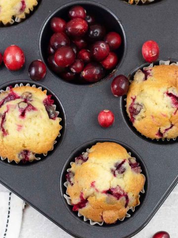Cranberry Muffins in a muffin tin along with fresh Cranberries.