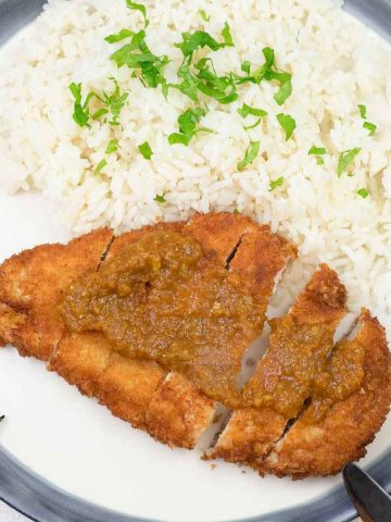 Chicken Katsu topped with Katsu curry on a plate with white rice.