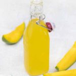 Mango syrup in a glass bottle and some fresh mango slices around it.