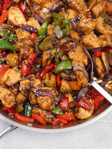 Chicken bell peppers onions stir fry in a skillet.