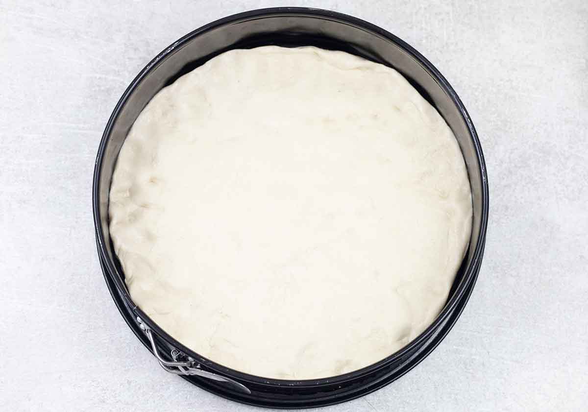 Roll out the pizza dough and place it in a round baking pan.