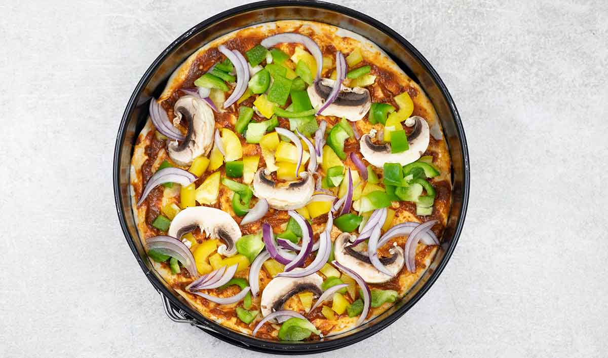 Spread the chopped onion, bell pepper, and mushroom evenly on the pizza.