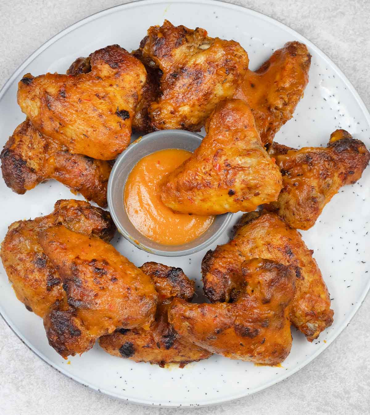 Mango habanero wings dipped in a bowl of sauce.