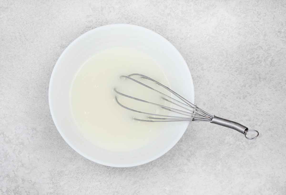 powdered sugar and milk mixed in a small bowl and a small whisk.