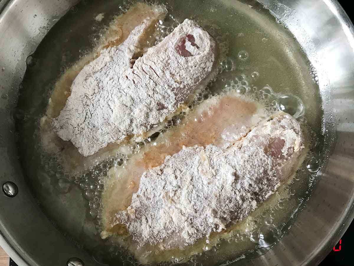 Frying two tilapia fillets in hot oil.