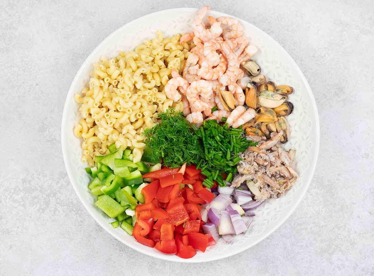 Cooked pasta, shrimp, mussels, chopped veggies, and herbs in a large serving salad bowl.